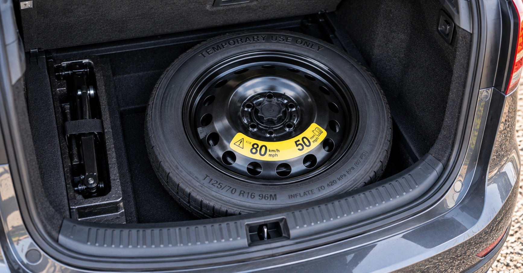 Space saver spare wheel in a car boot showing the temporary-use maximum speed warning